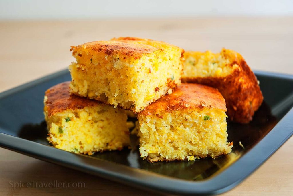 Four square pieces of Texas corn bread with cheese on black plate.