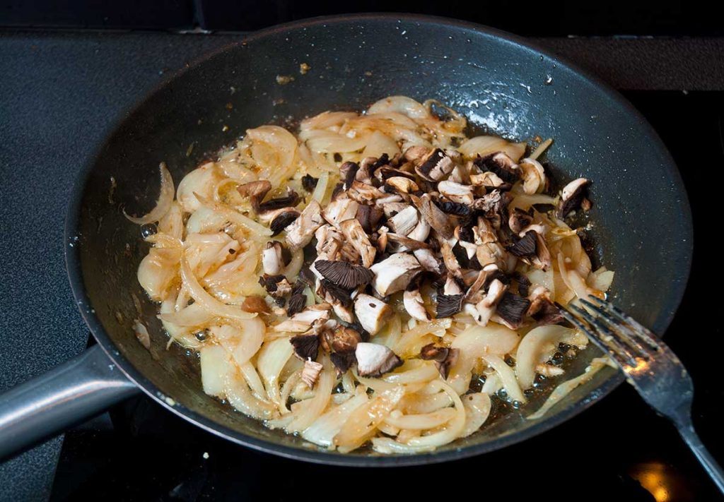 Adding chopped mushrooms to onions and garlic.