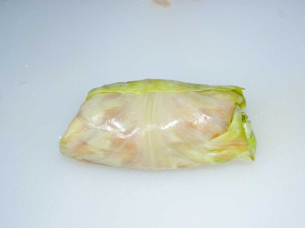 Polish stuffed cabbage leaf parcel with the sides tucked in, fully enclosing the filling , ready to cook.