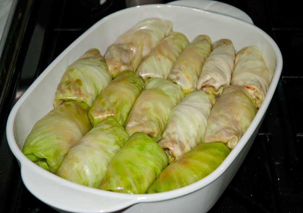 Golabki neatly arranged in a baking dish, ready to be topped with shredded cabbage leaves and liquid for baking.