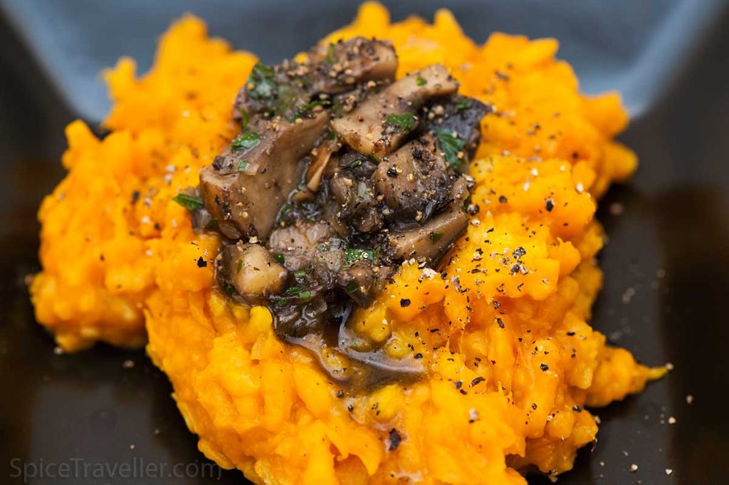 Close up of delicious roasted pumpkin risotto in a black bowl, topped with fried dark mushrooms.