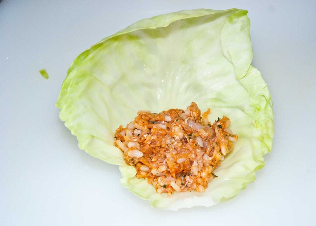 A spoonful of meat and rice mixture placed at the beginning of a cabbage leaf, ready for rolling into golabki.