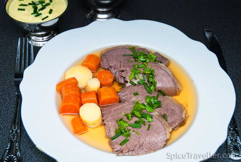 Austrian Tafelspitz slices served with carrot and parsnip with goden broth and garnished with parsley and chives.