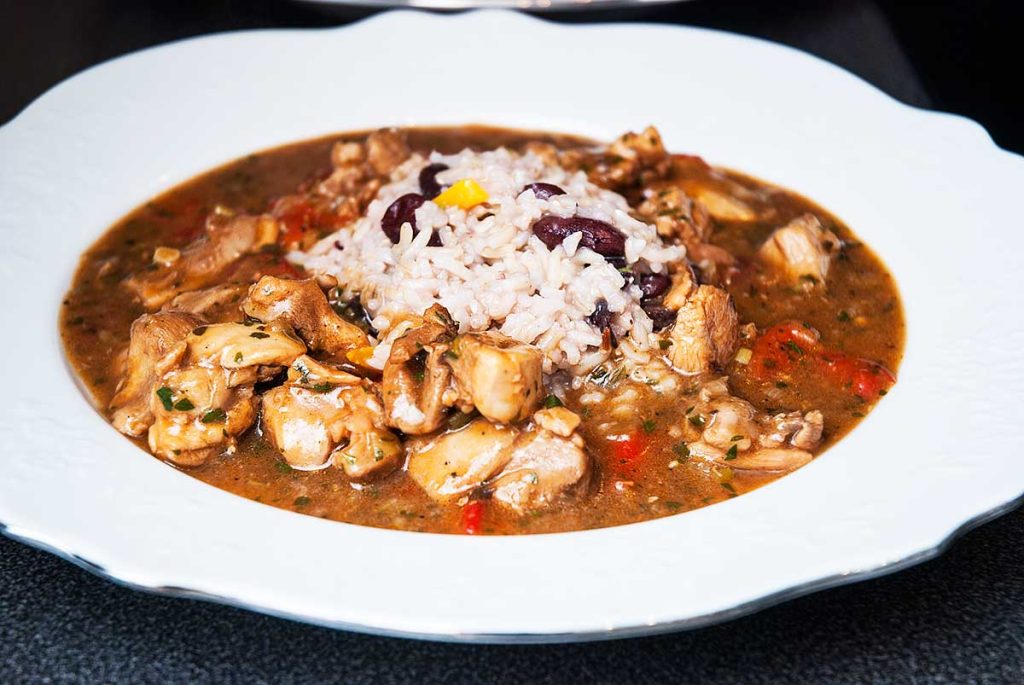 White plate full of simple Caribbean spicy brown chicken stew served with fluffy coconut rice and beans.