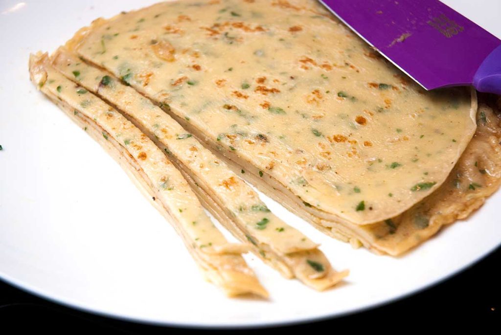 Cutting stack pancakes with chives into thin ribbons for Austrian soup. 