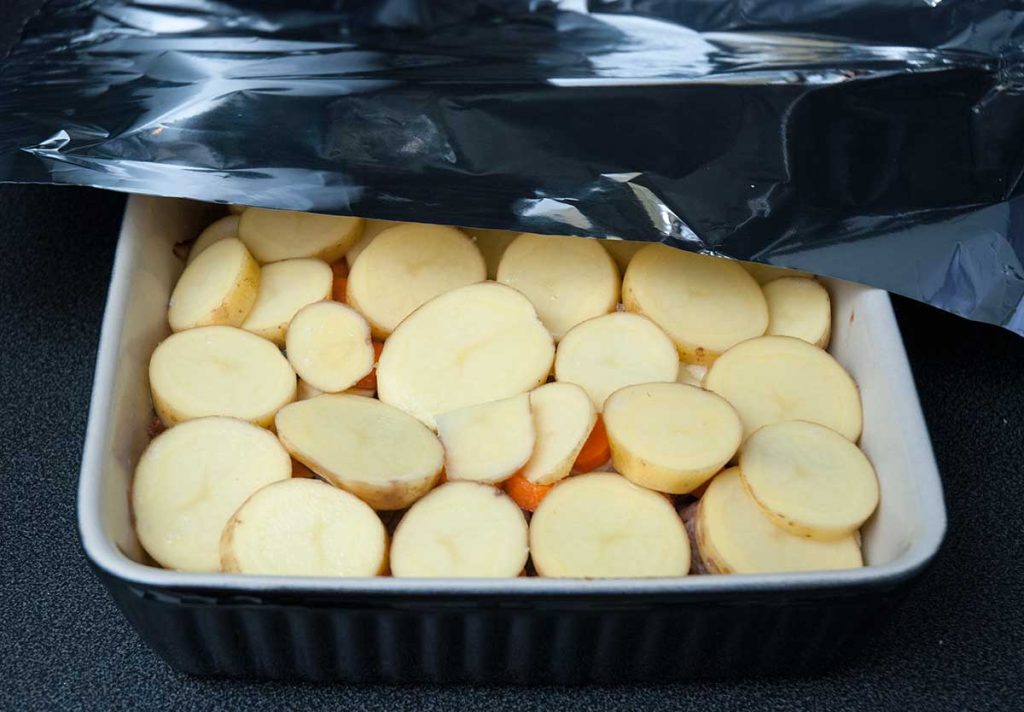 Covering lamb and potato bake dish with foil before baking.