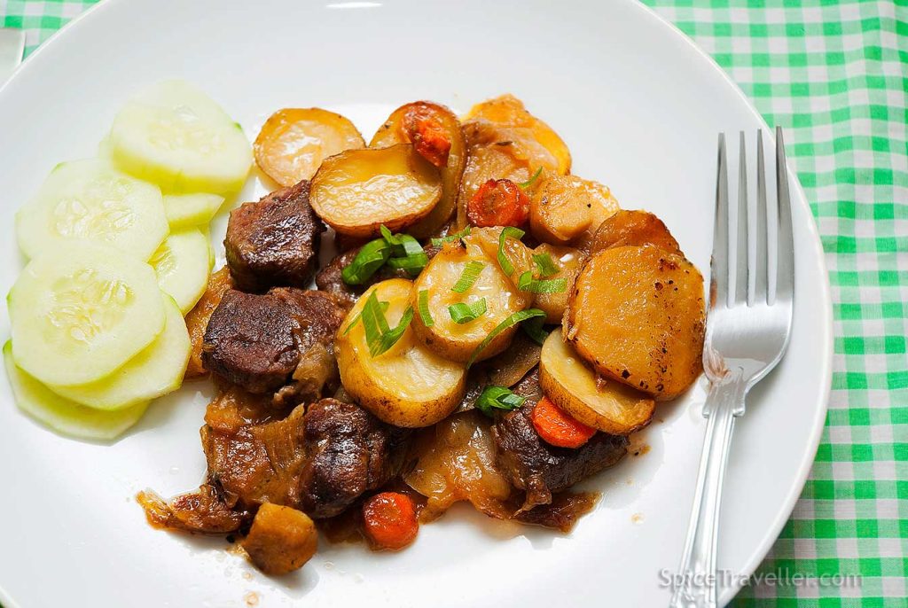 Serving suggestion: Perfectly baked, delicious looking slices od potato, chunks of lamb and vegetables served on white plate with a few slices of cucumber placed on a side.