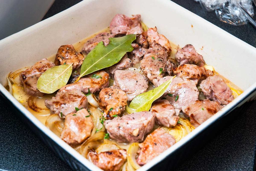 Assembling lamb and potato bake dish, adding layer of meat.