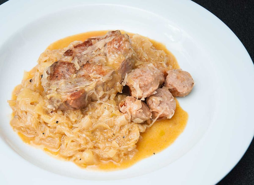 Pork steak with sausage pieces and sauerkraut served on white plate.