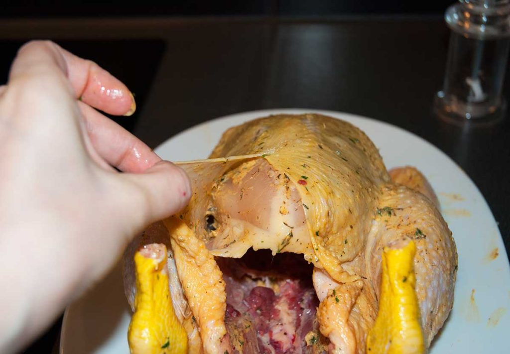 Showing butter spread over chicken breast undreneath the skin.