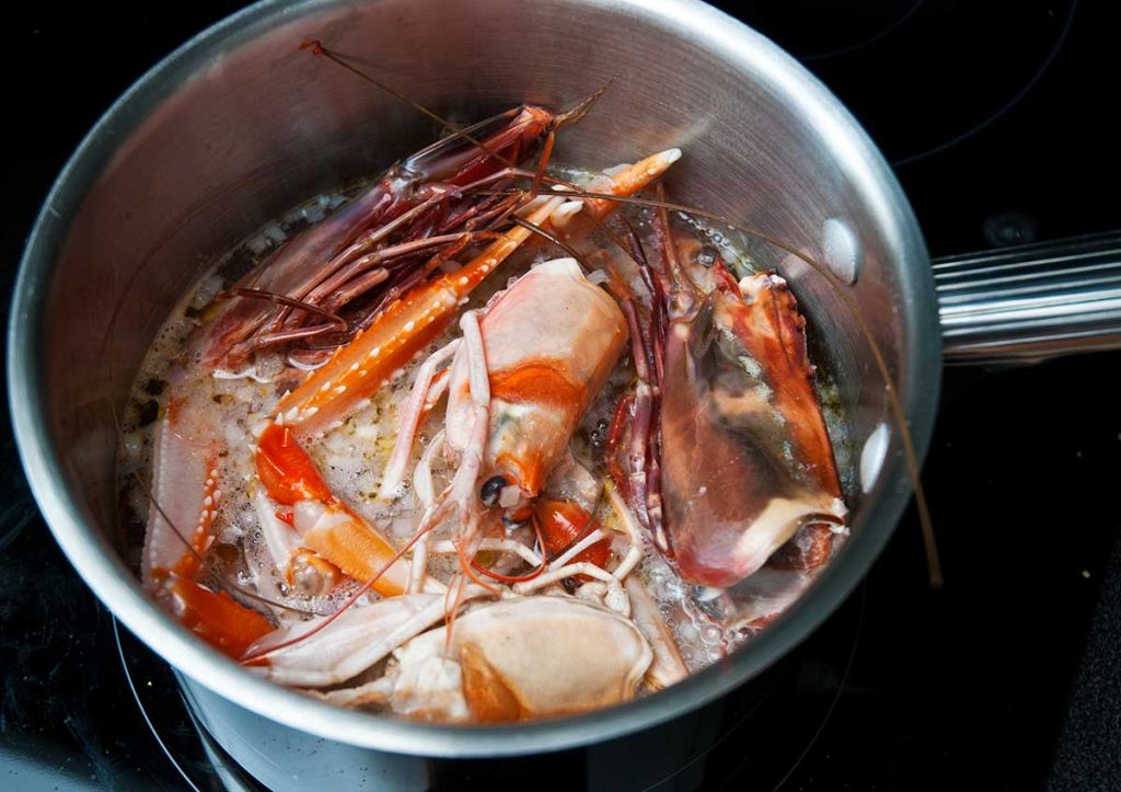 Boiling langoustine and king prawn heads in a metal pot.