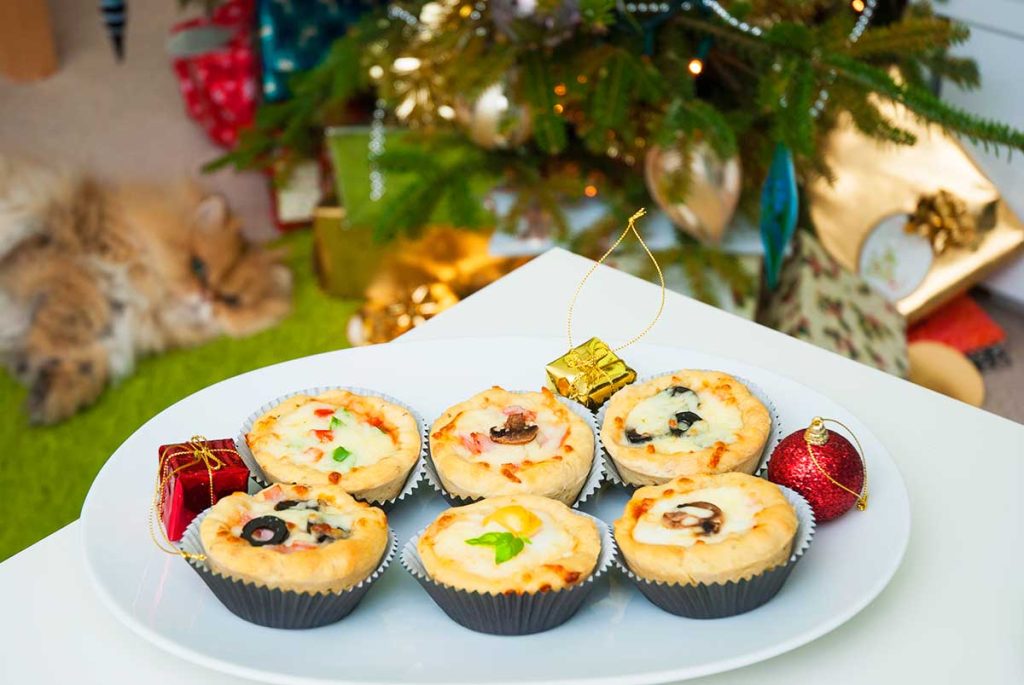 Festive looking mini pizza cucpakes served on a plate with Christmas tree in the background.