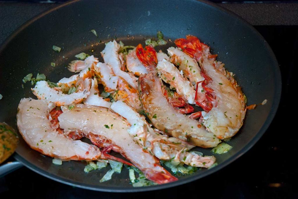 Searing halved langoustine and prawn tails in a frying pan.