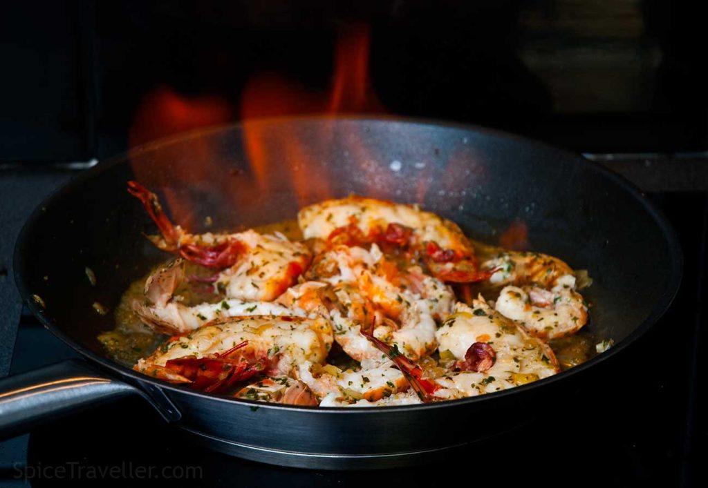 Flambéing langoustines and prawns in a hot pan with fire and flames for a dramatic cooking effect.