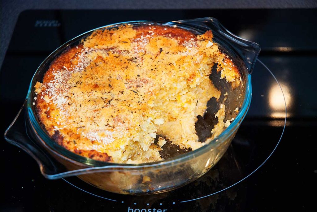 Mashed root vegetable bake in a clear baking dish with a serving already taken out, showing a golden, crispy breadcrumb topping.