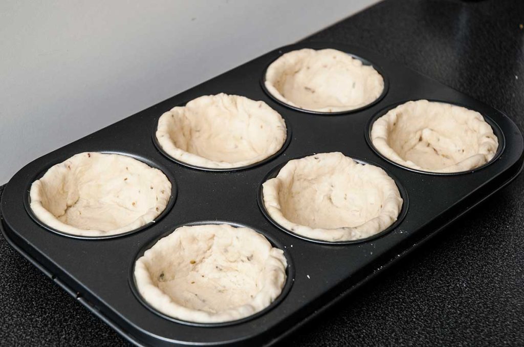 Mini pizza cupcake dough pressed into muffin tin holes, ready to pre-bake.