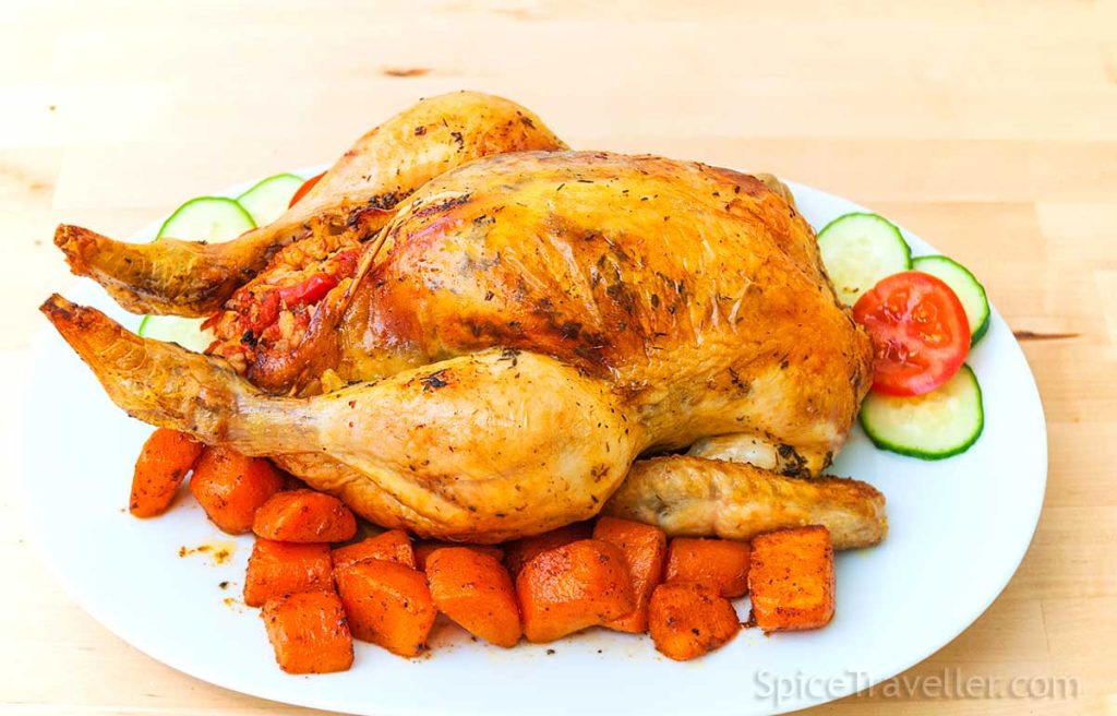 Serving whole stuffed chicken on a large oval plate with carrots and cucumber slices.