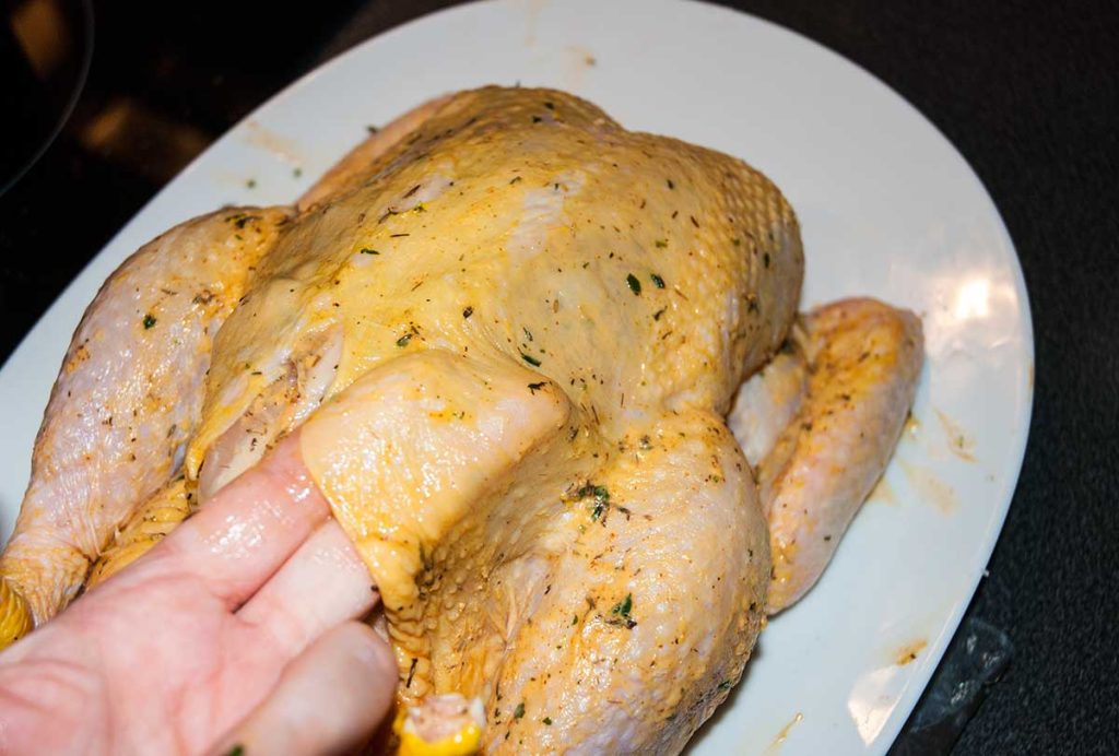 Showing how to lift chicken skin to spread the butter.