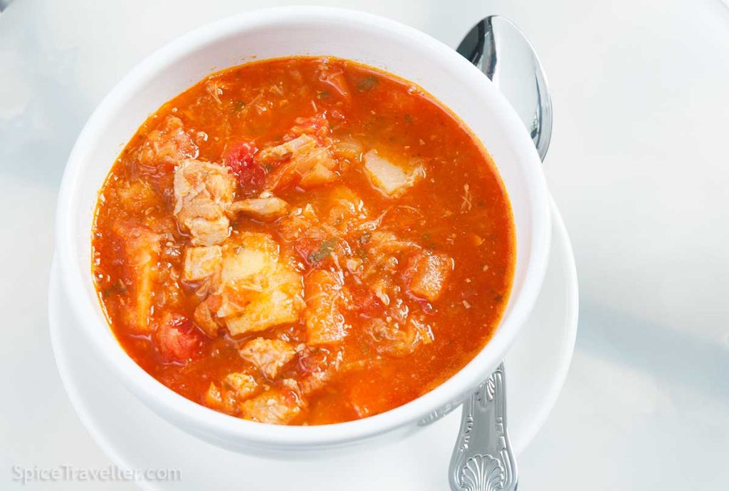 Szekely goulash variation - white bowl full of hearty hungarian pork, potato and sauerkraut stew with tomato sauce.