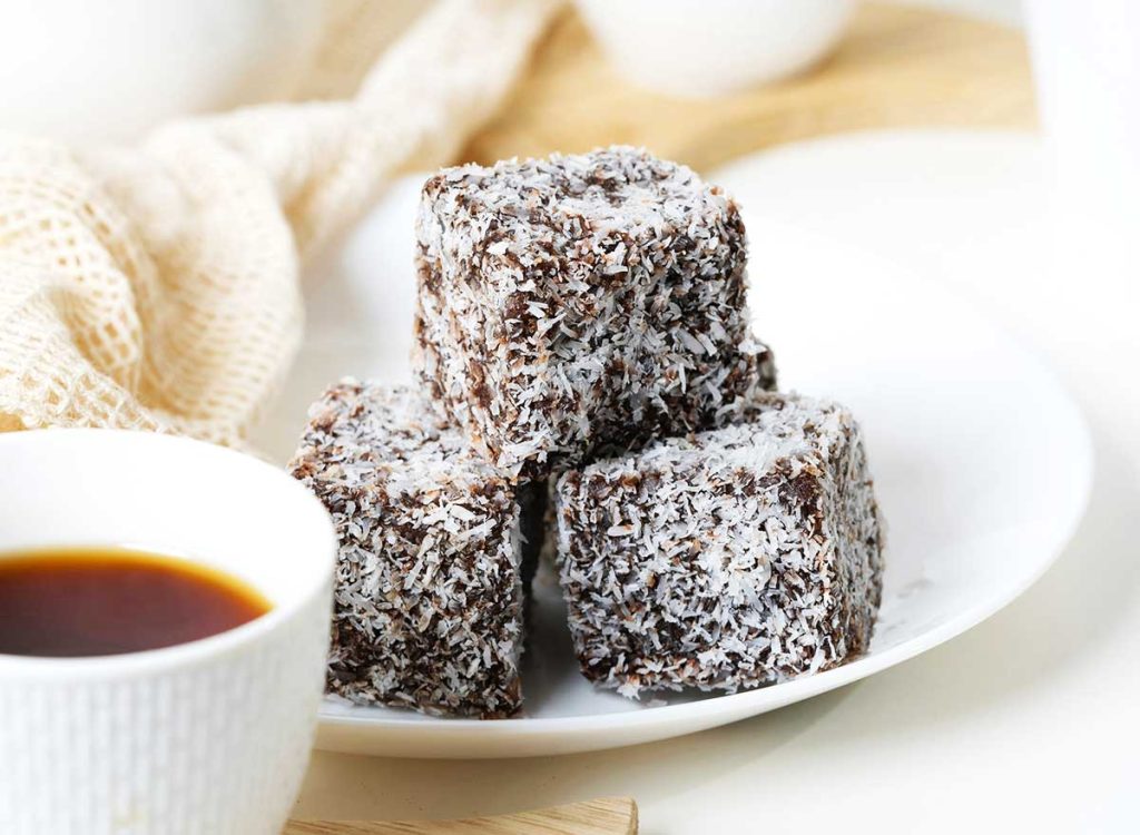 Classic Lamingtons served on a white small plate next to a cup of coffee.