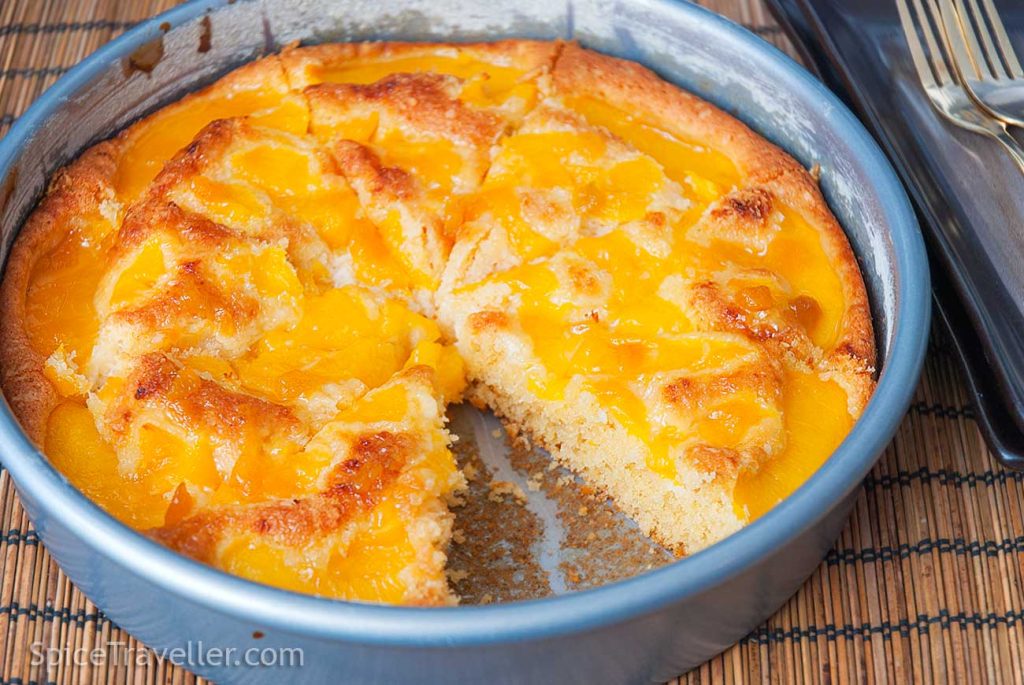 Round baking dish with freshly baked coconut and peach cake pie with one cut out slice.