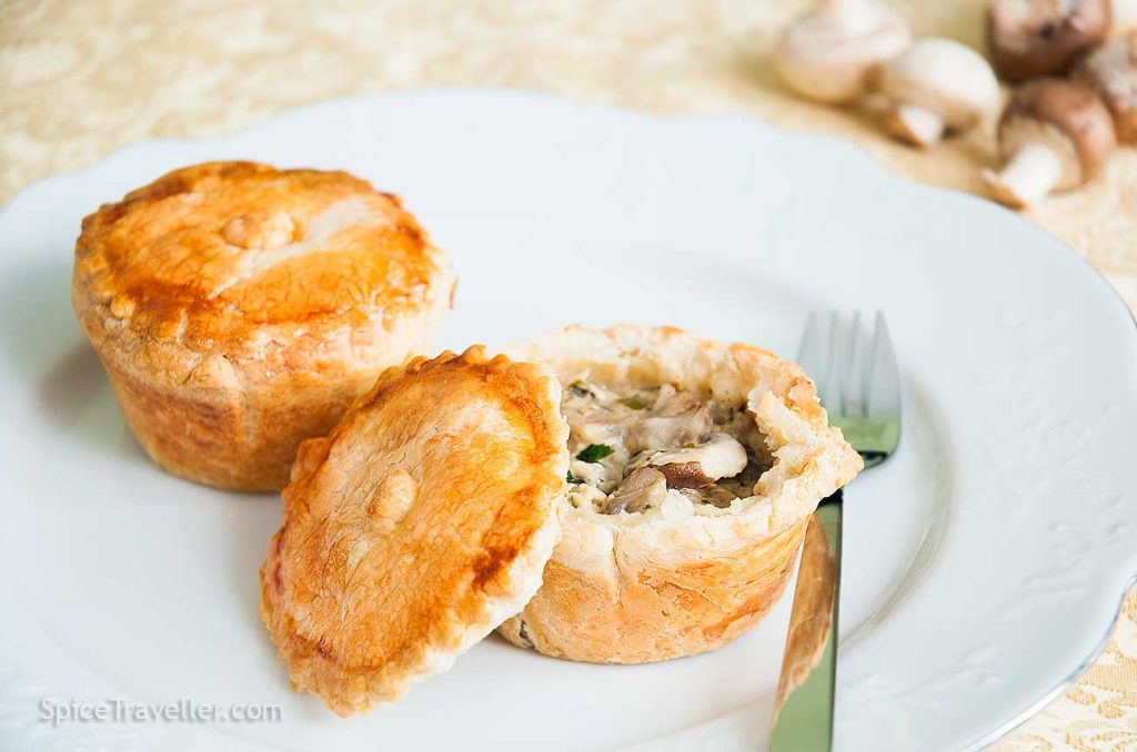 Two freshly baked mini chicken and mushroom pies served on a white plate, one with the pastry lid off, revealing its delicious filling.