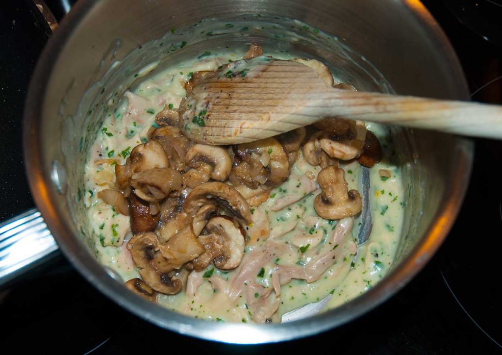 Shredded chicken mixed with roux and fried mushrooms in a pot.