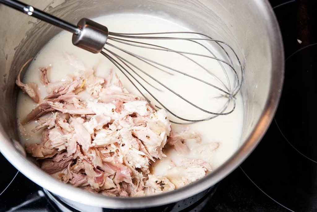 Shredded roast chicken mixed with roux in a pot.