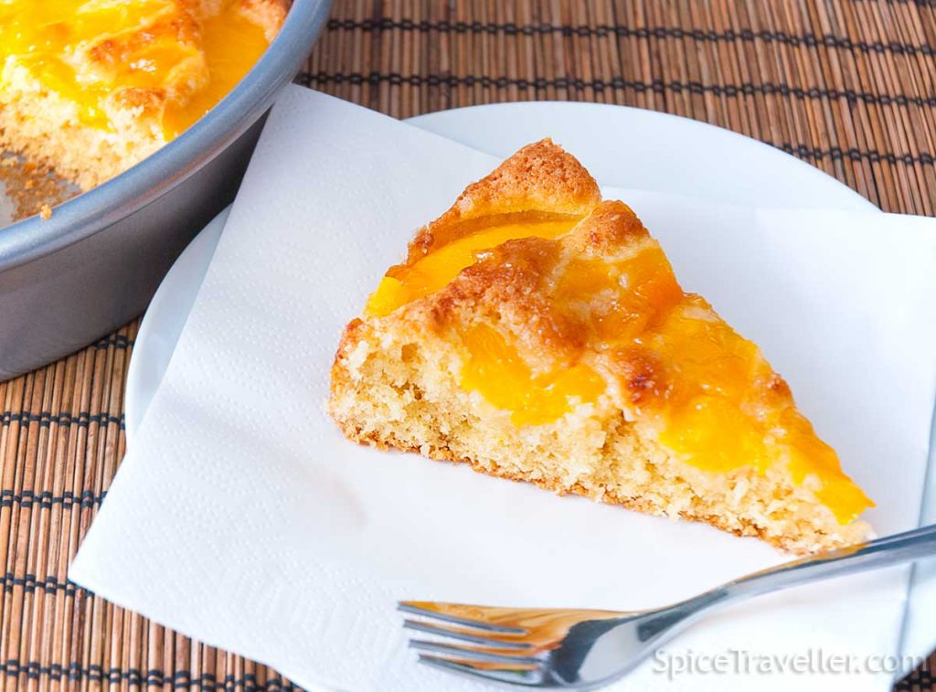 Close up of one slice of coconut and peach cake pie served on a white napkin and white plate. 