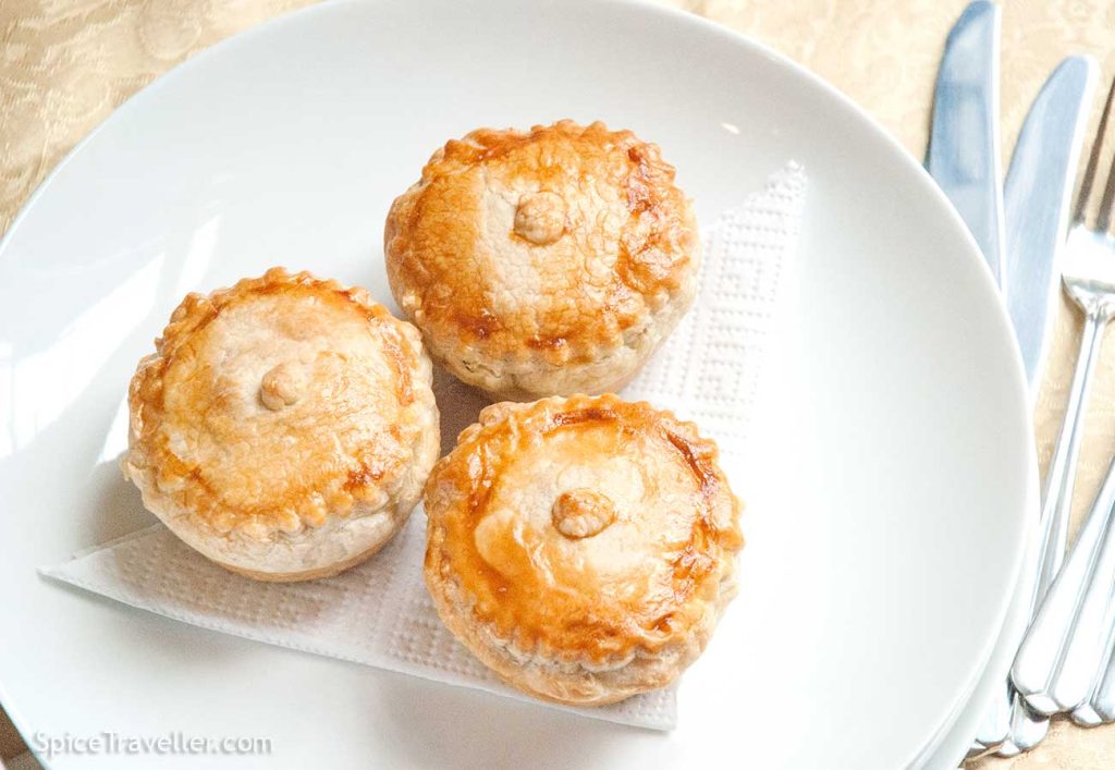 Three perfectly baked mini chicken and mushroom pies elegantly served on a white plate.