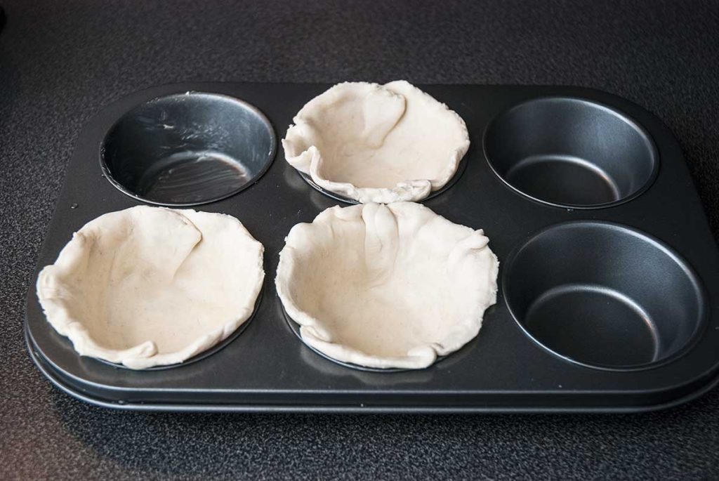 Placing round puff pastry dough pieces in cupcake tray moulds.