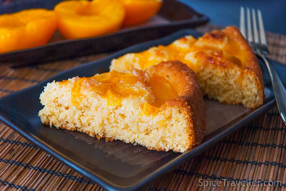 Close up of two juicy peach and coconut cake pie slices on black plate.