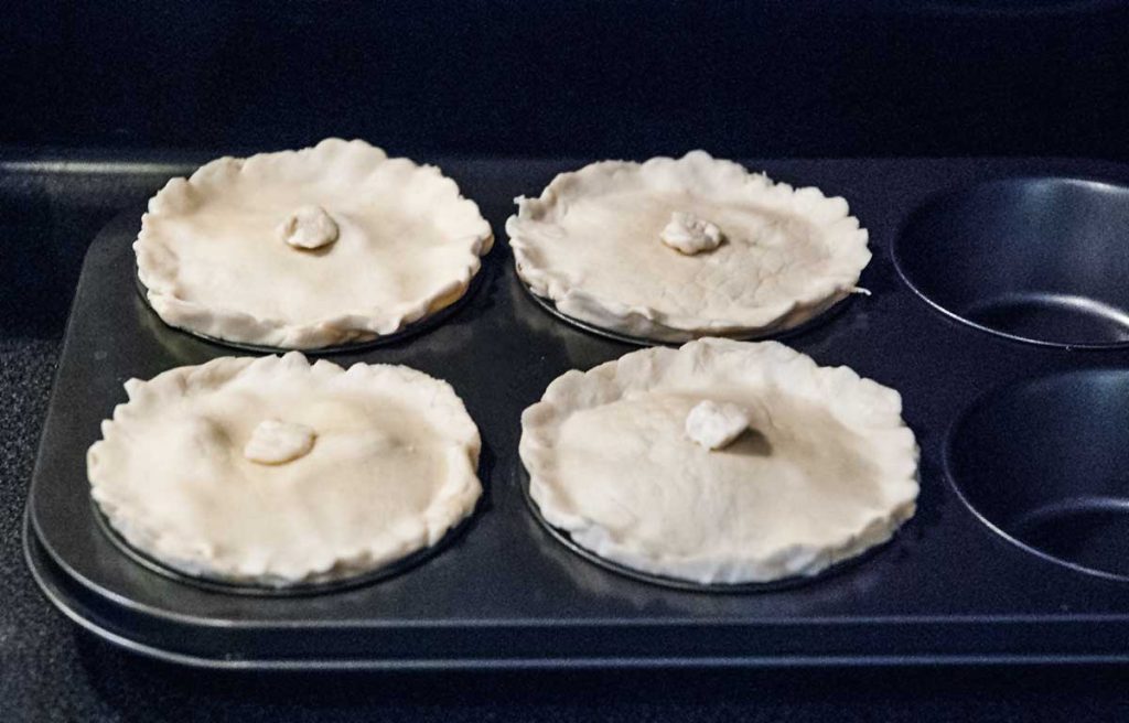 Mini pies covered with puff pastry lids, ready to bake.