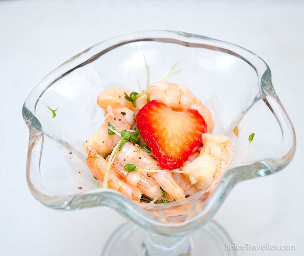 Close up of a seafood cocktail with strawberry and Prosecco dressing, garnished with cress and a slice of strawberry resembling a heart.