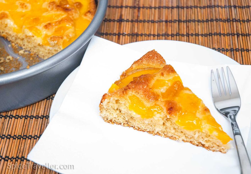 One coconu and peach cake pie slice on a white plate with juicy glazing. 