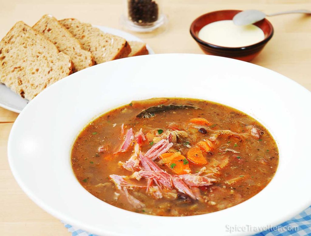 Slovak Kapustnica - sauerkraut and pork hearty soup served in a large white bowl with brown bread and sour cream.