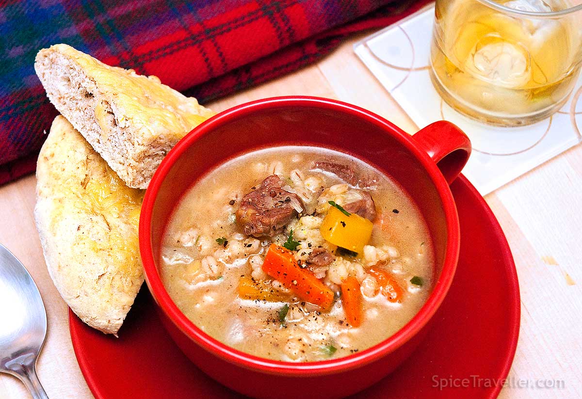 Red soup cup full of hearty Scotch Broth served with Bannock bread.