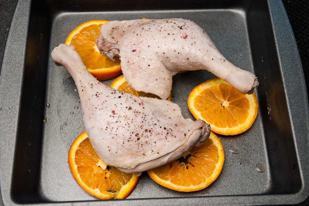 Chicken legs with orange slices ready to roast.