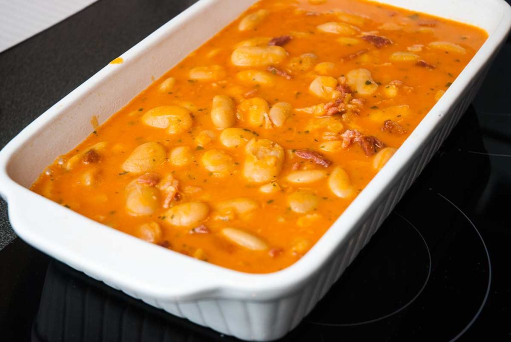 Butter beans in sauce transferred to a white rectangular baking dish, ready to bake.