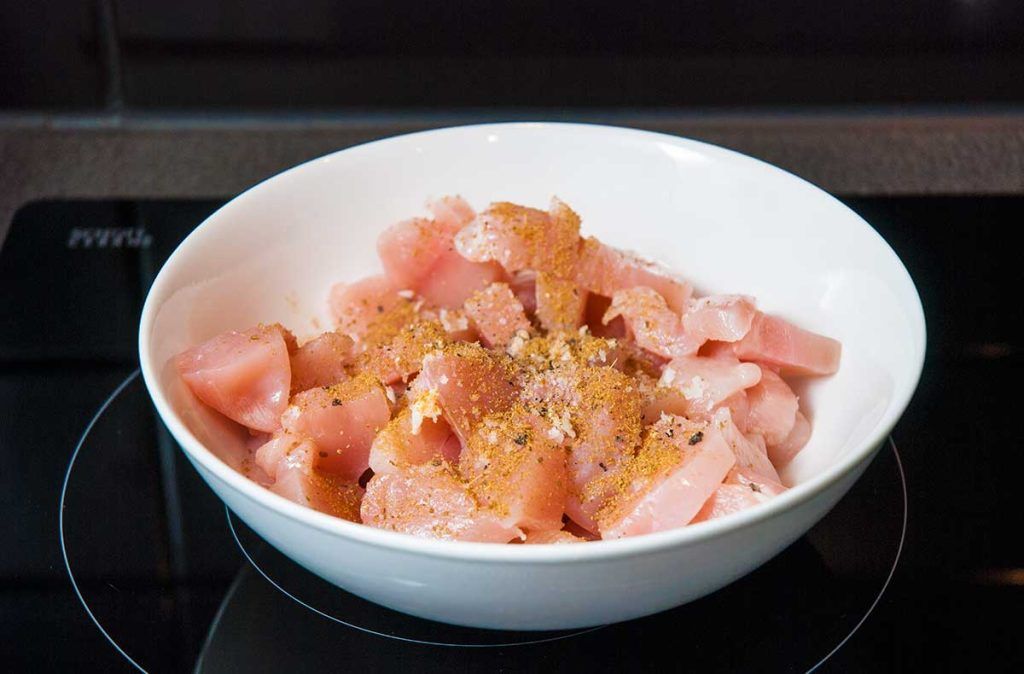 Bowl of raw chicken breast pieces mixed with spices.