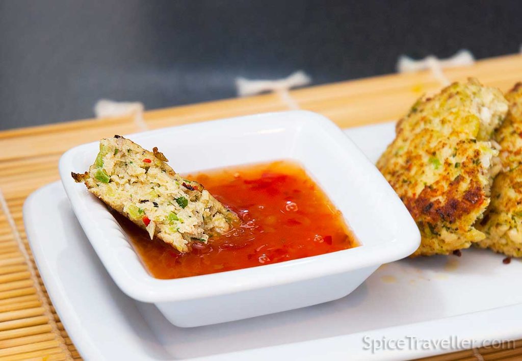 Close up of Thai spicy chicken burger piece showing the texture, dipped in sweet chilli sauce.