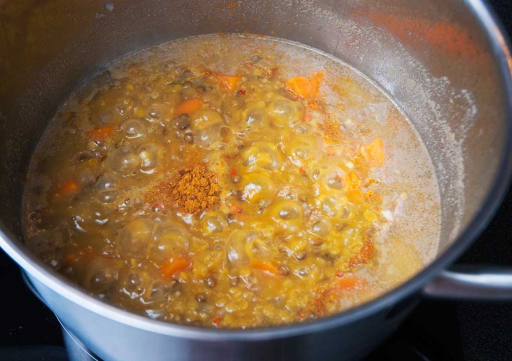 A pot of Arabic lentil and lamb mince soup simmering, with visible lentils, carrots, and spices, creating a hearty, bubbling mixture.