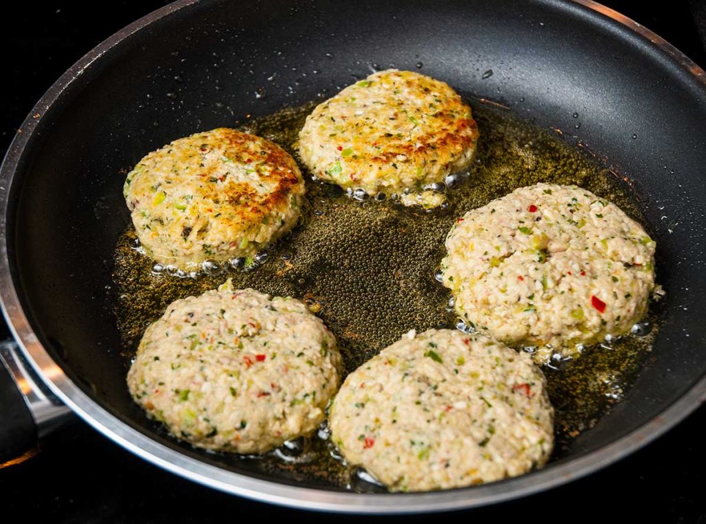 Five Thai chicken burgers shallow frying in a pan.