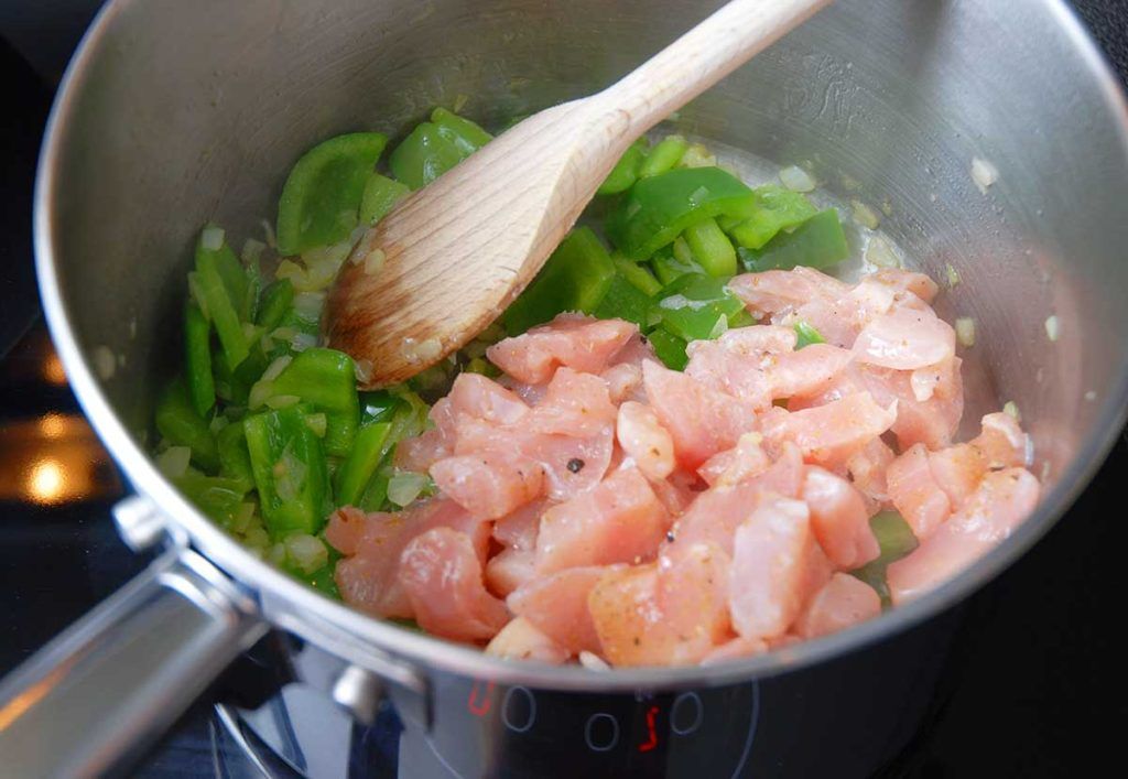 Frying chicken pieces with peppers for perfect galinhada.