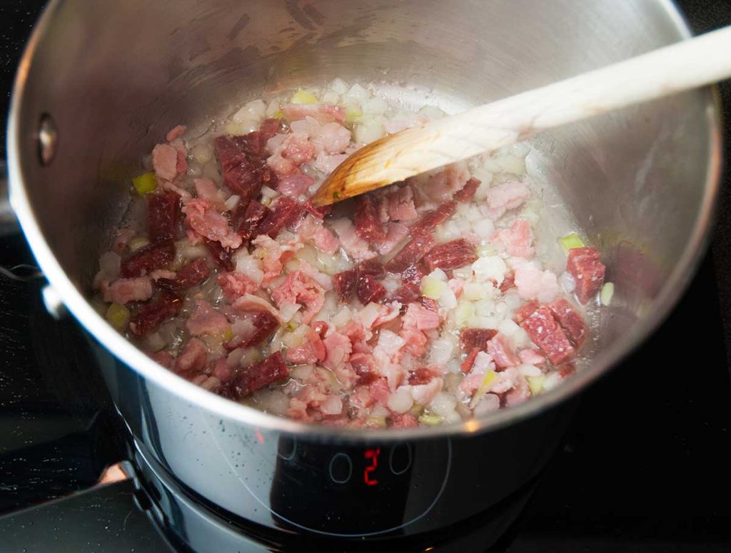 Frying finely chopped onion, bacon and sausage in a pot.