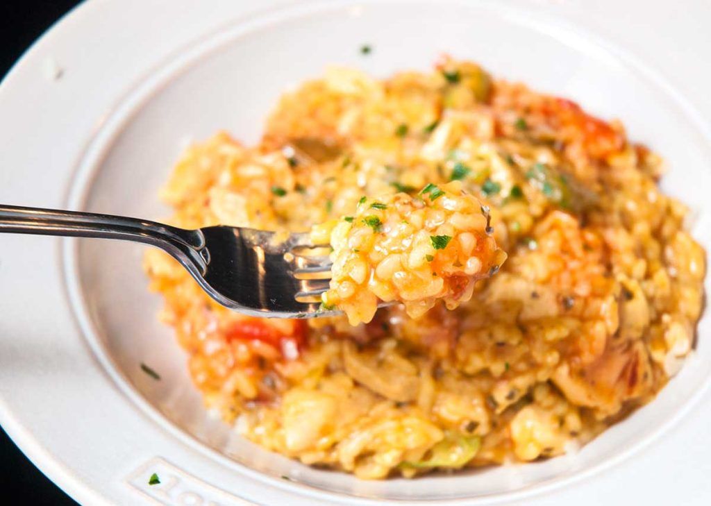 Close up of delicious Brazilian Galinhada (chicken and peppers with rice) on a fork garnished with chopped parsley.