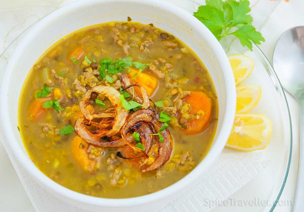 Hearty lamb and lentil soup garnished with caramelized onions and fresh parsley, served with lemon wedges.