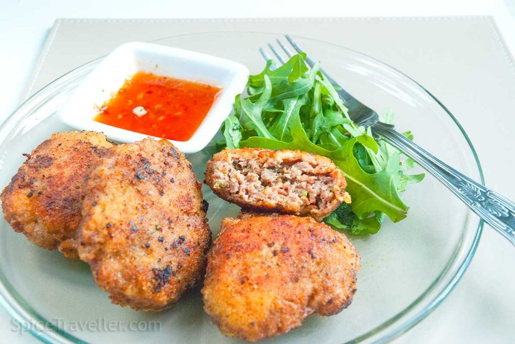 Australian rissoles ( beef patties) with one cut in half showing the soft inside texture, served with sweet chilli dipping sauce and wild rocket leaves.