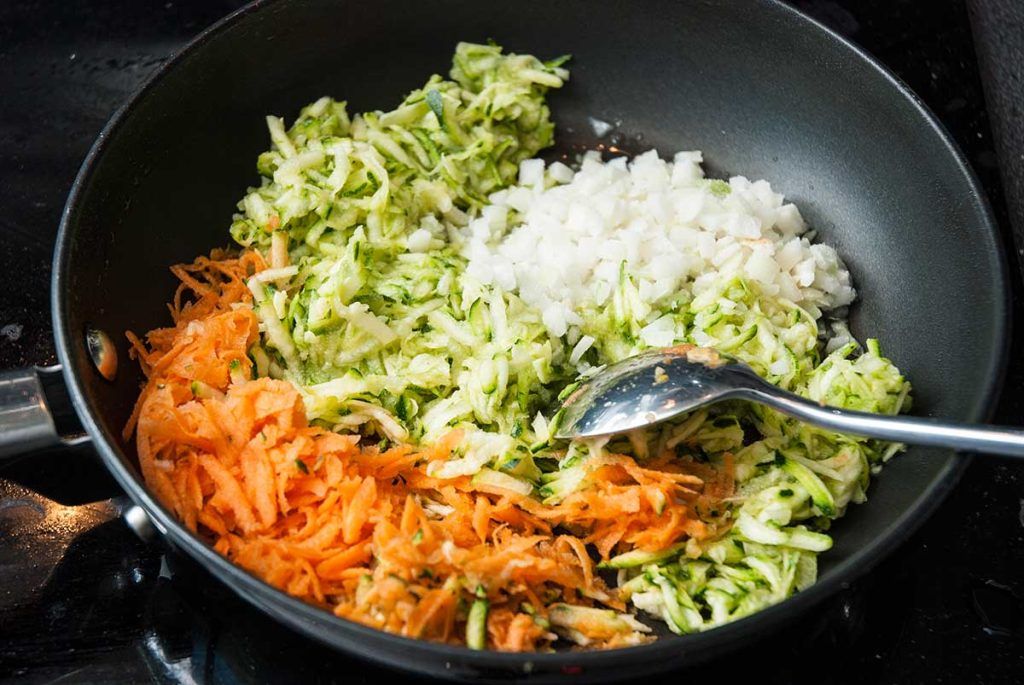 Frying grated courgettes and carrots with finely chopped onion.