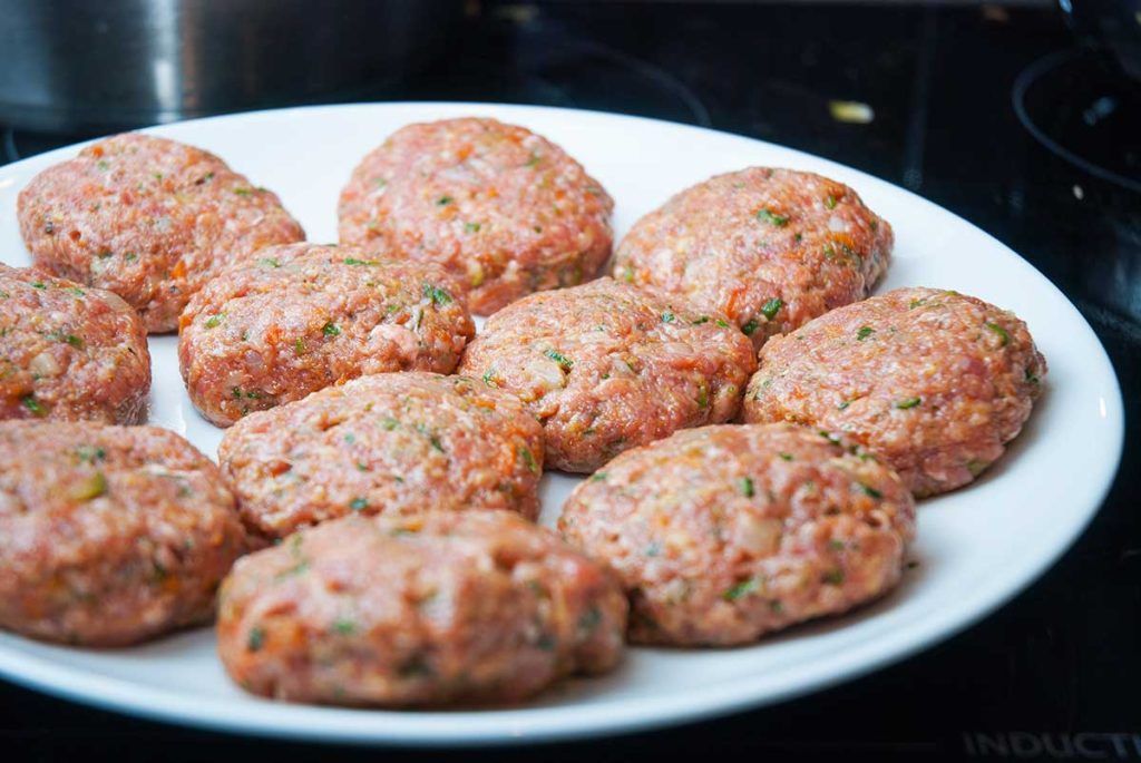 Shaped Australian rissoles on a white plate ready to fry.